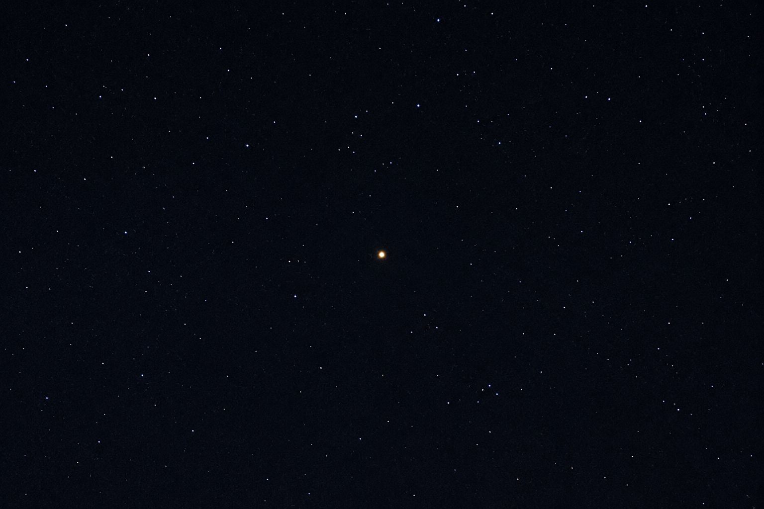 Saturn as a bright yellow point of light in the night sky, photographed from Earth