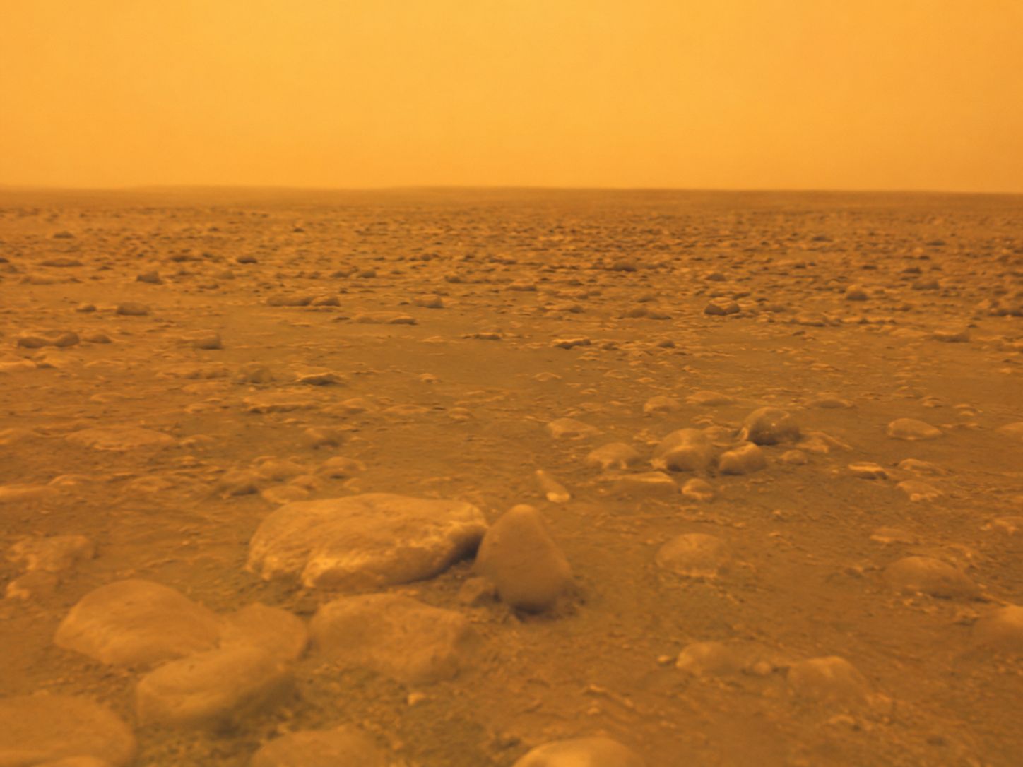 The surface of Titan photographed by the Huygens probe in January 2005, showing pale rounded rocks of water ice on an orange plain